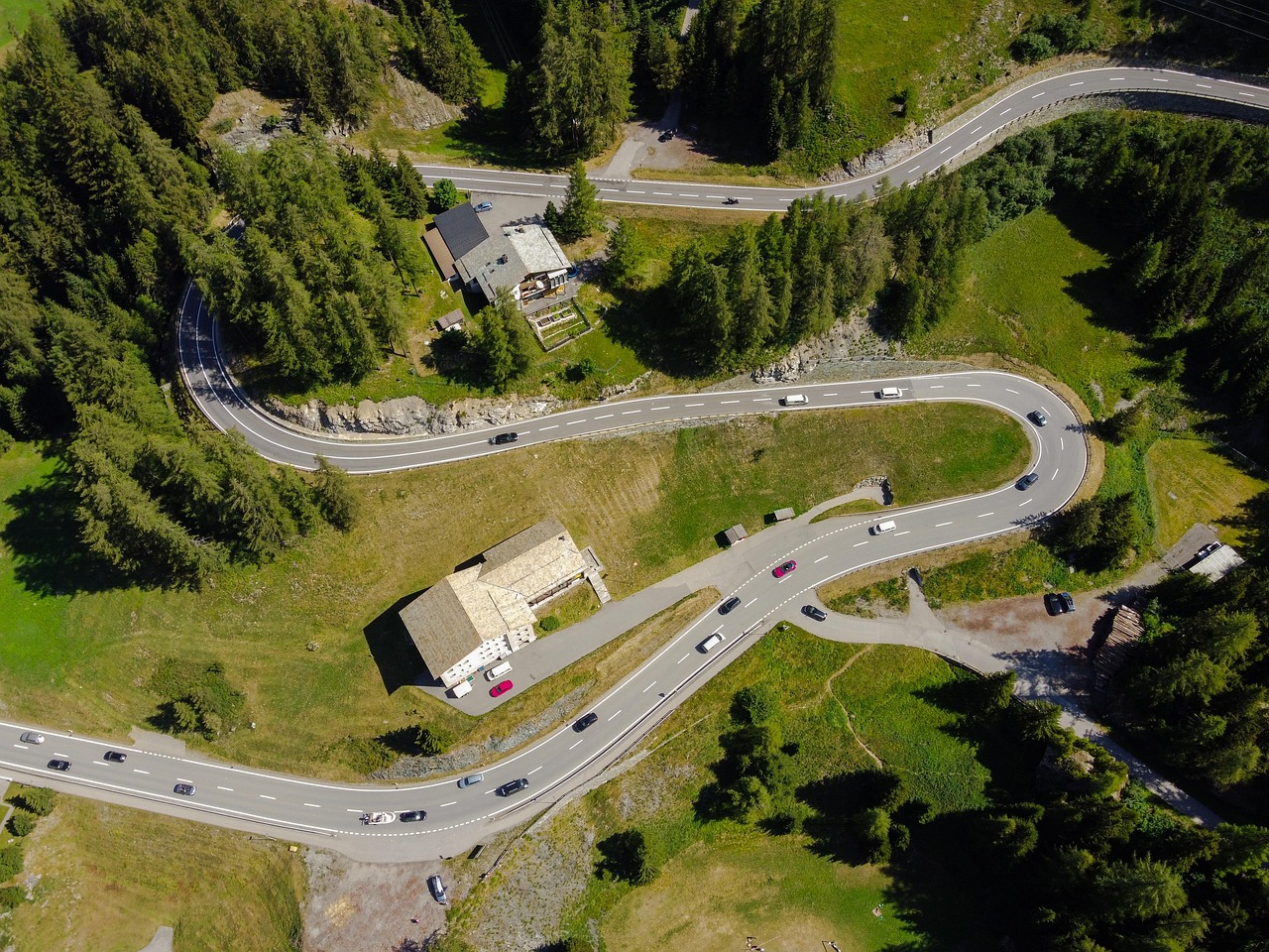 A winding road, small buildings, and forested landscape photographed from above