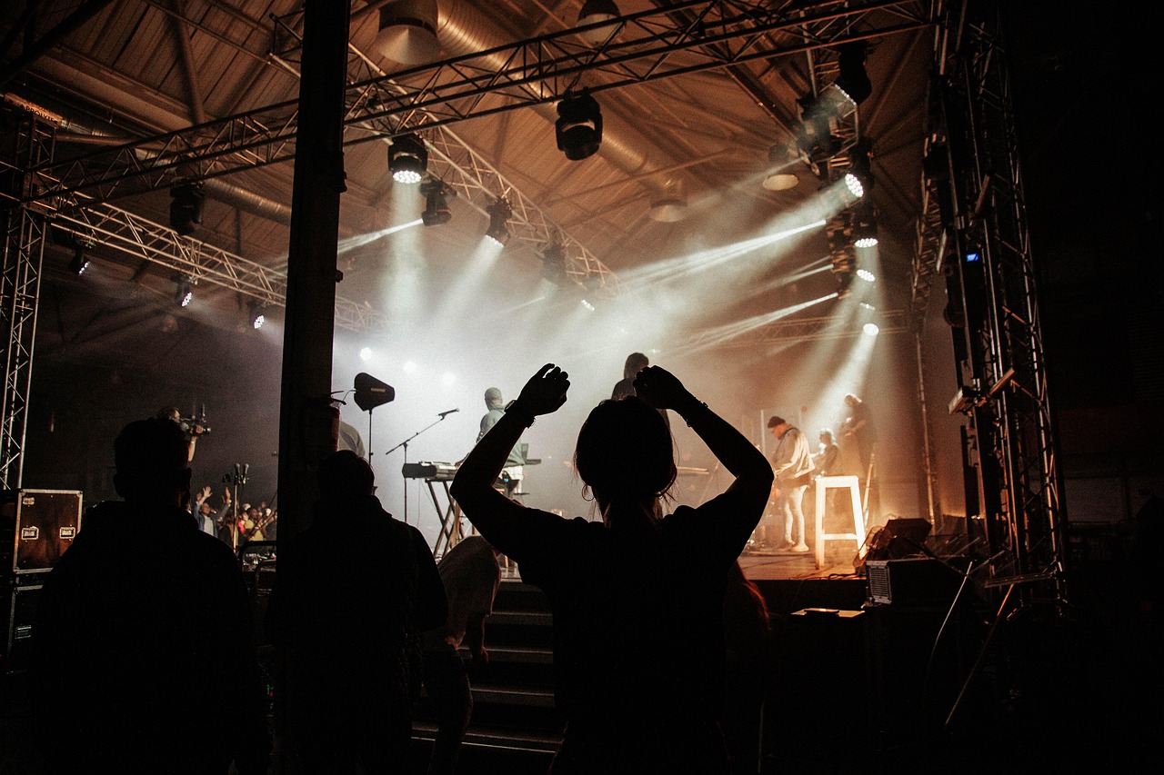 Silhouetted concertgoers raising their hands beneath golden stage lights