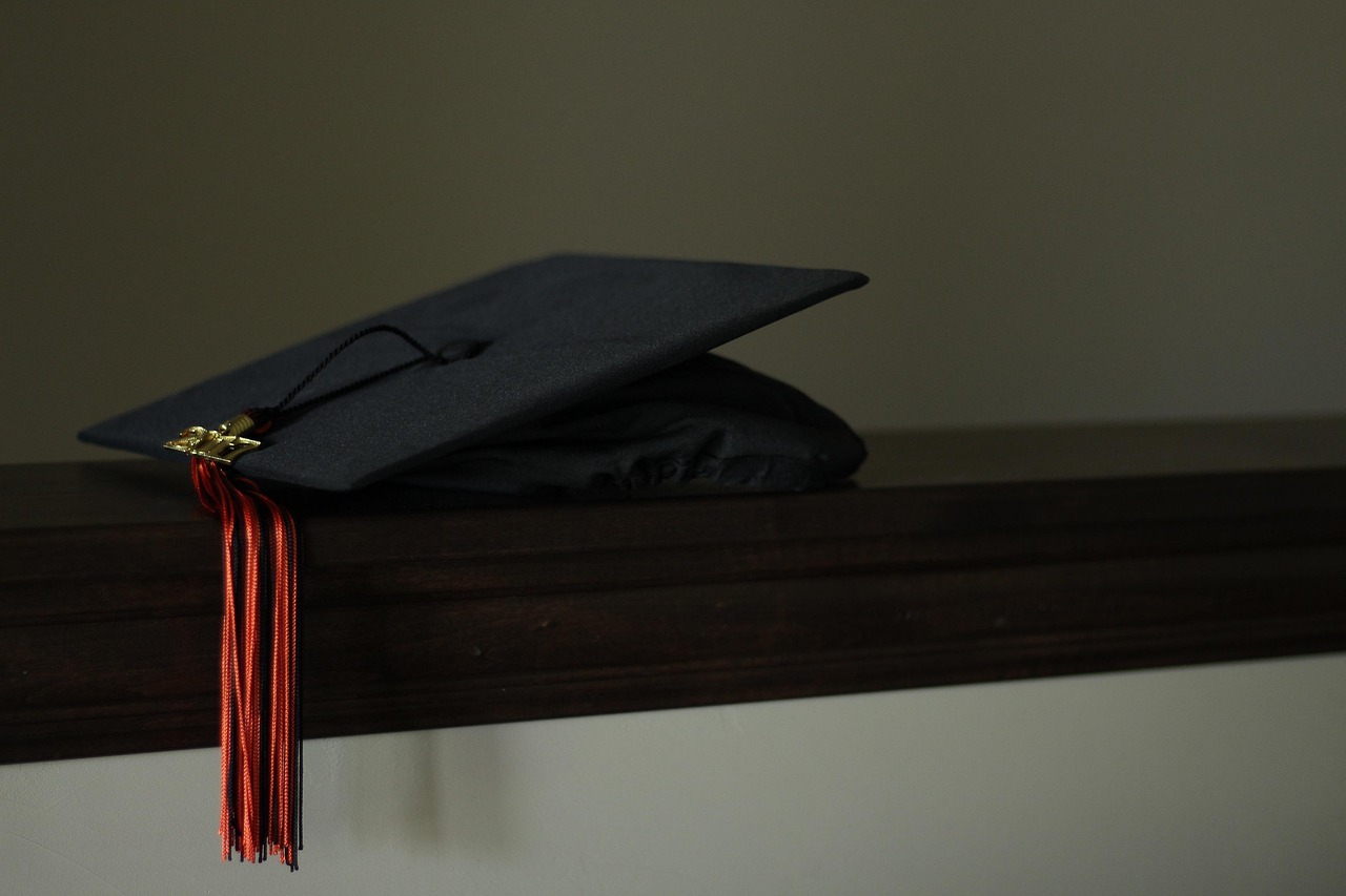 A black graduation cap with a red tassel resting on a wooden ledge