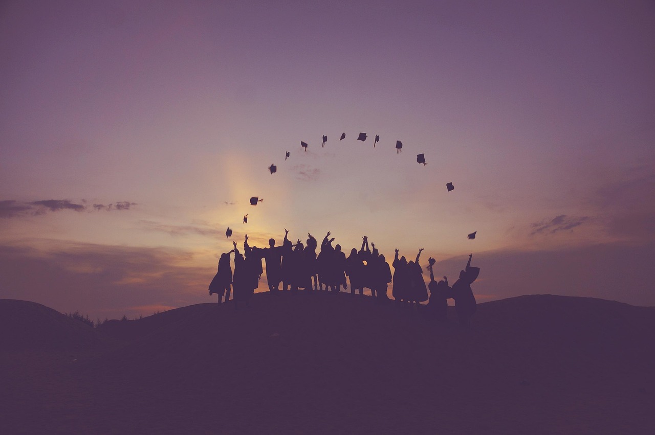 Silhouetted graduates throwing their caps into the sunset sky