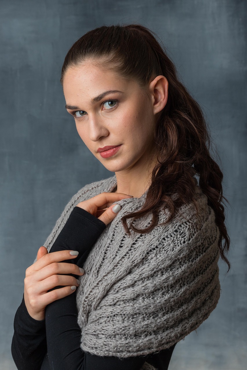 A woman in a gray knitted scarf photographed against a soft gray studio background