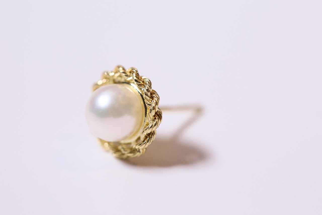 Gold jewelry with a large pearl photographed on a pale lilac background