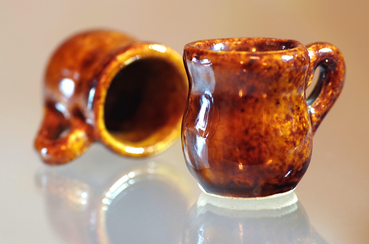 Two amber-glazed ceramic cups arranged on a reflective pale surface