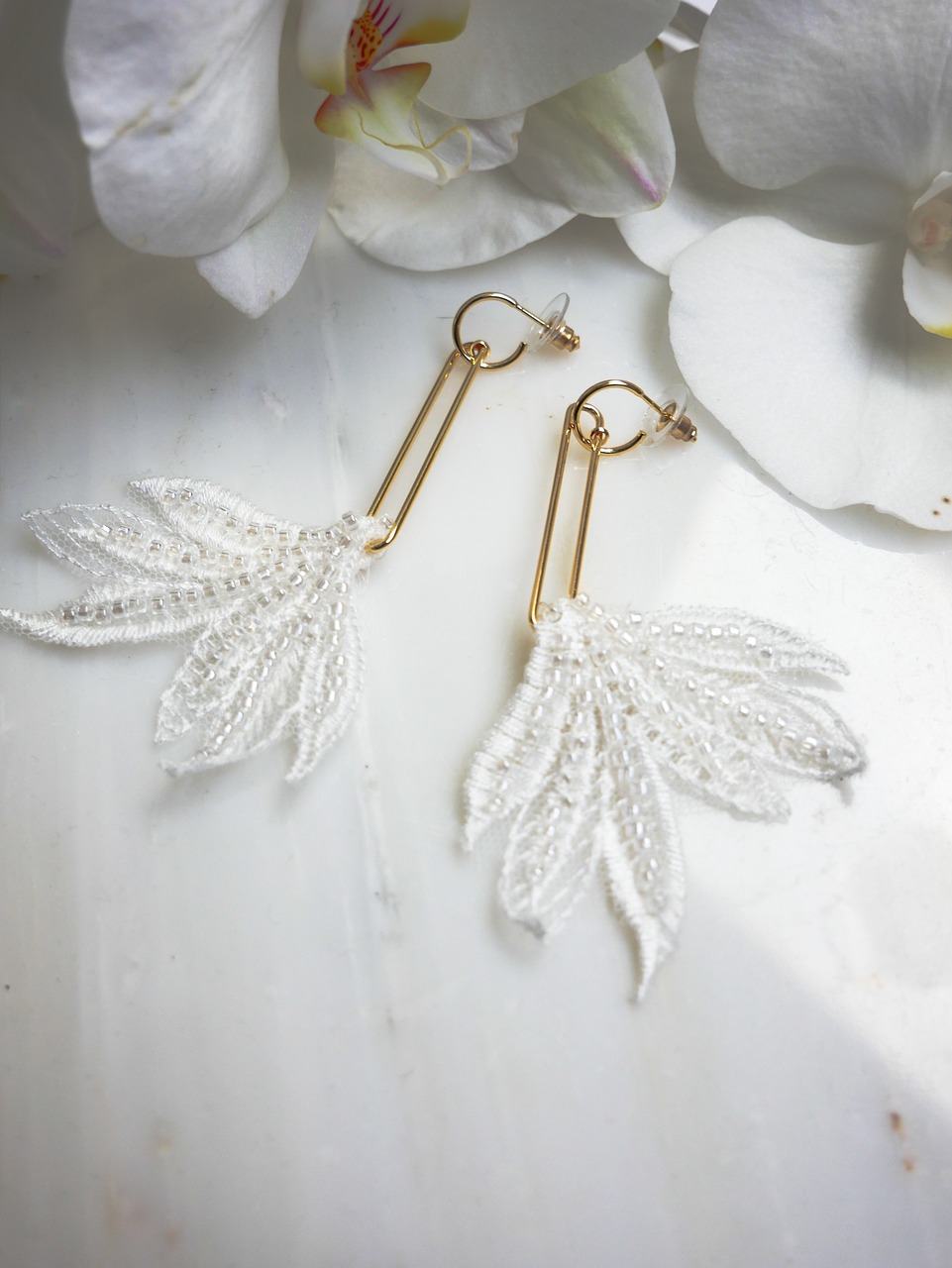 White beaded leaf-shaped earrings arranged beside an orchid