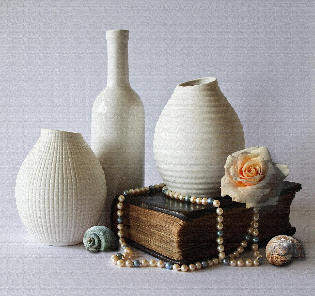 White ceramic vases arranged with a rose, shells and beads