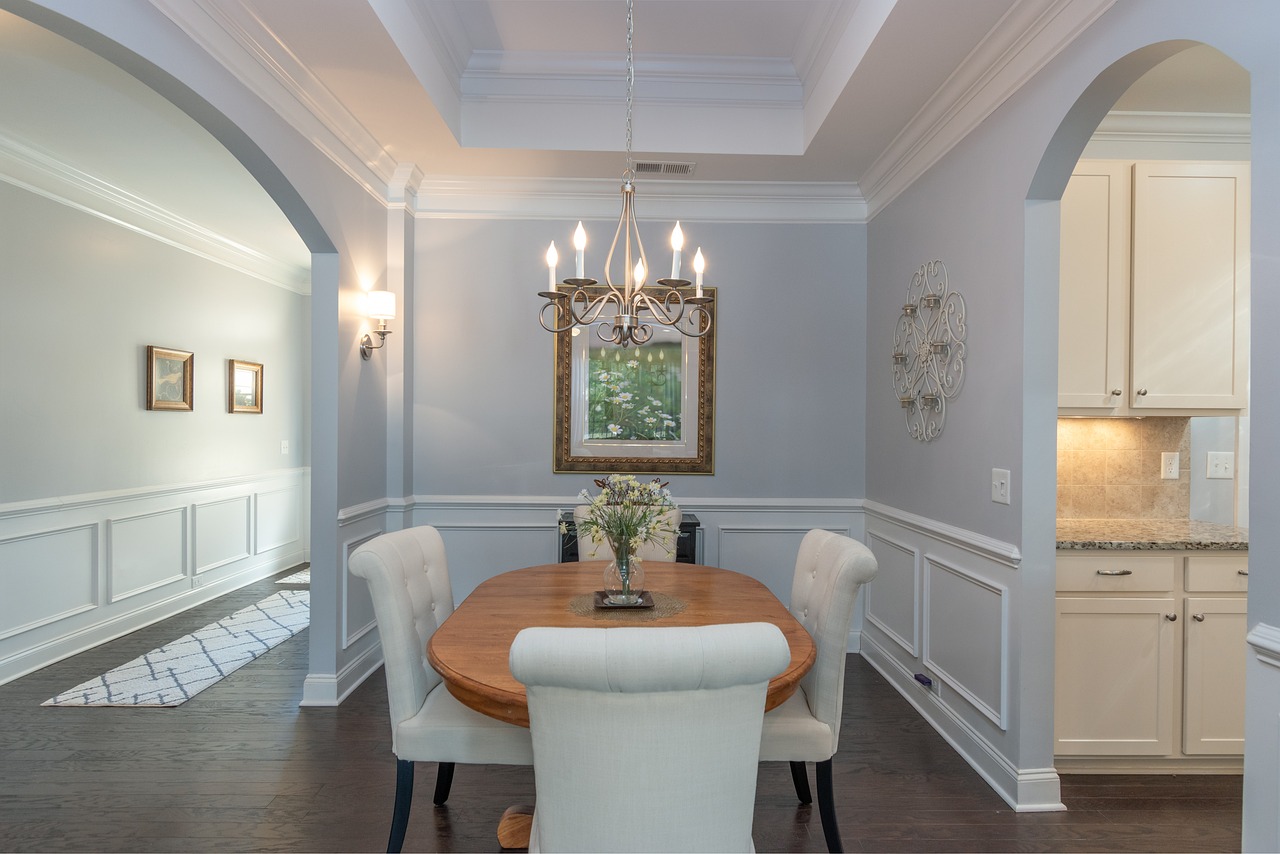 A pale blue dining room with wall paneling, a chandelier and upholstered dining chairs