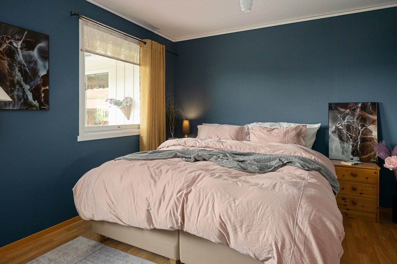 A bedroom with deep blue walls, soft pink bedding and natural window light