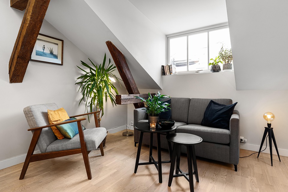 A compact sitting room with sloped ceilings, exposed beams, a gray sofa and houseplants