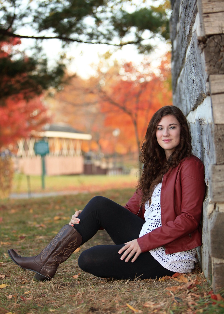 A young woman in a red jacket sitting beside a stone wall in autumn