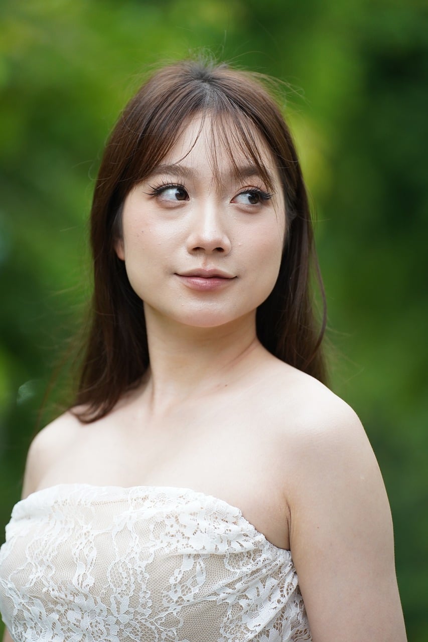 A young woman in a white formal dress posing against a green garden background