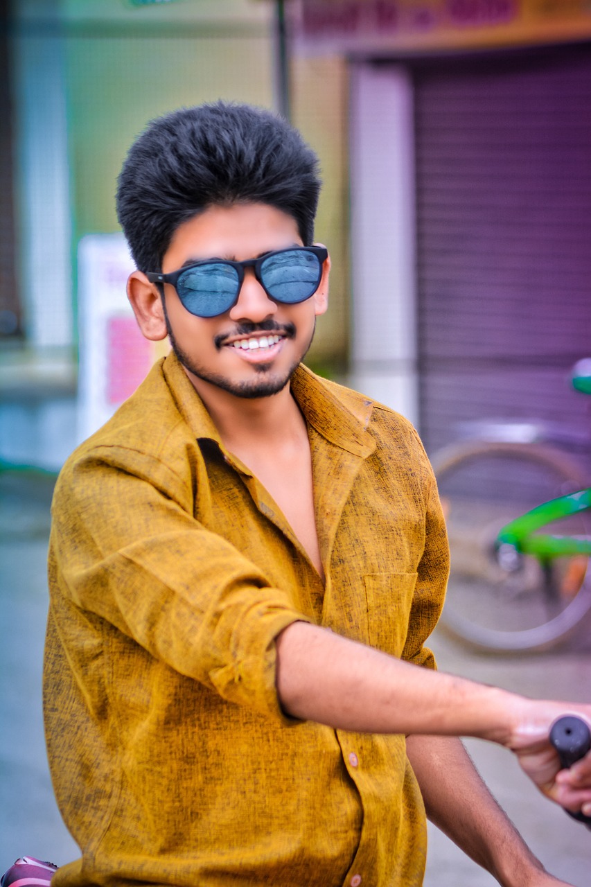 A young man wearing a mustard shirt and blue sunglasses in an outdoor portrait