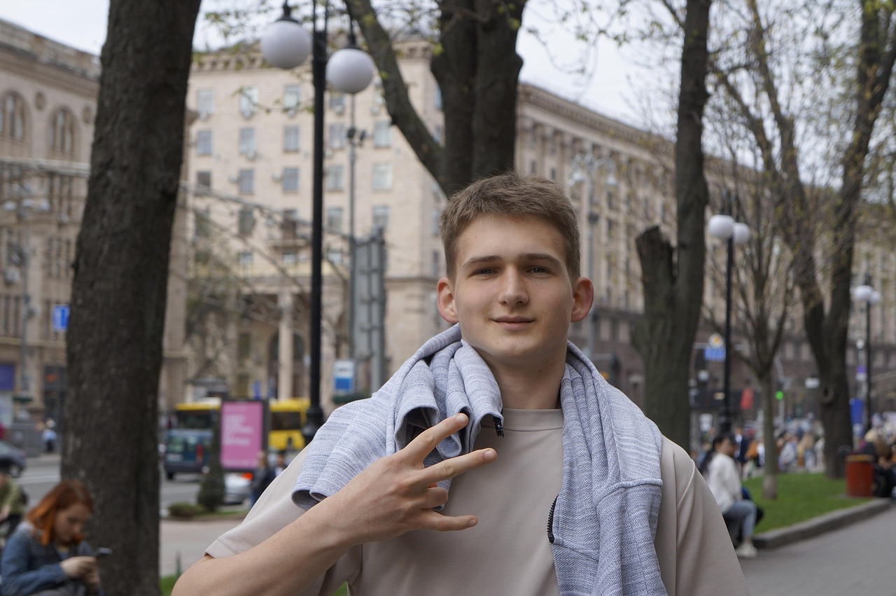 A young man in a white T-shirt and checked shirt posing on a tree-lined city street