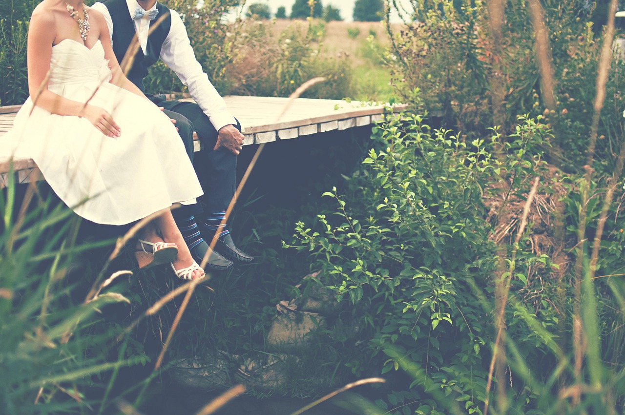 A newlywed couple sitting together on a wooden bridge surrounded by greenery