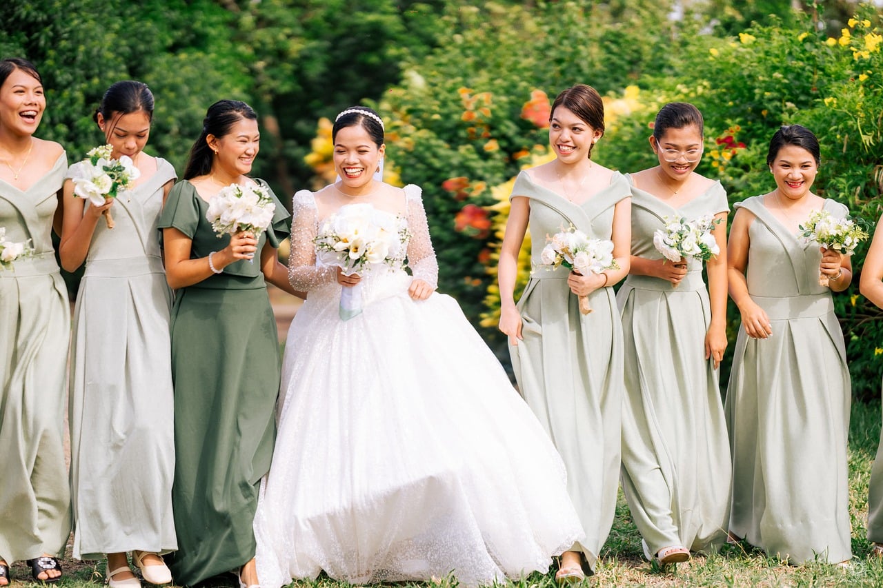 A bride and her bridesmaids in pale green dresses standing together in a garden