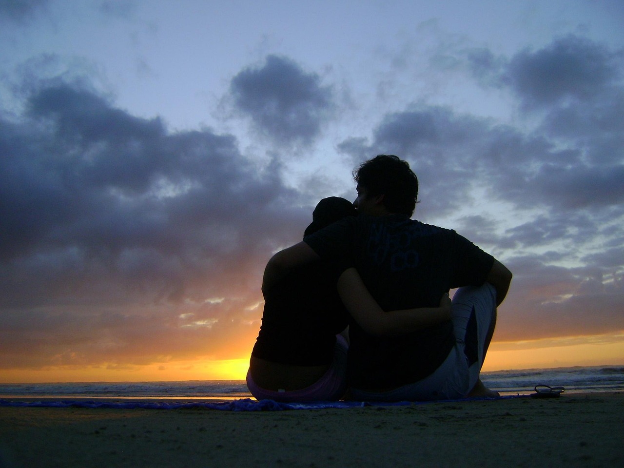 A couple sitting close together on a beach at sunset